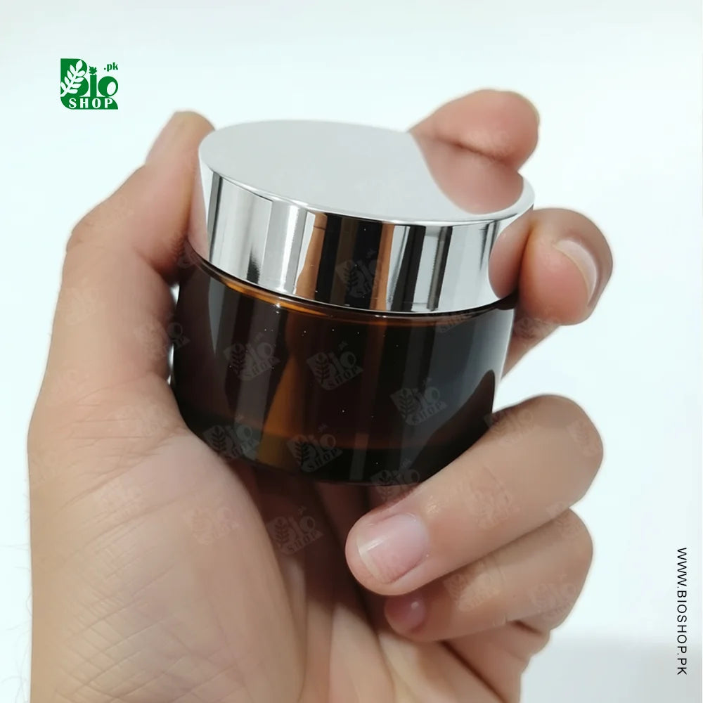Hand holding a dark glass jar with a silver lid against a white background, featuring the Bio Shop logo.