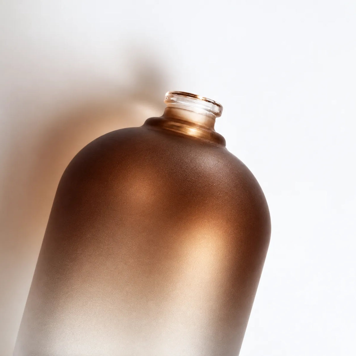 Close-up of the exposed crimp neck and rounded shoulders of a brown frosted glass perfume bottle